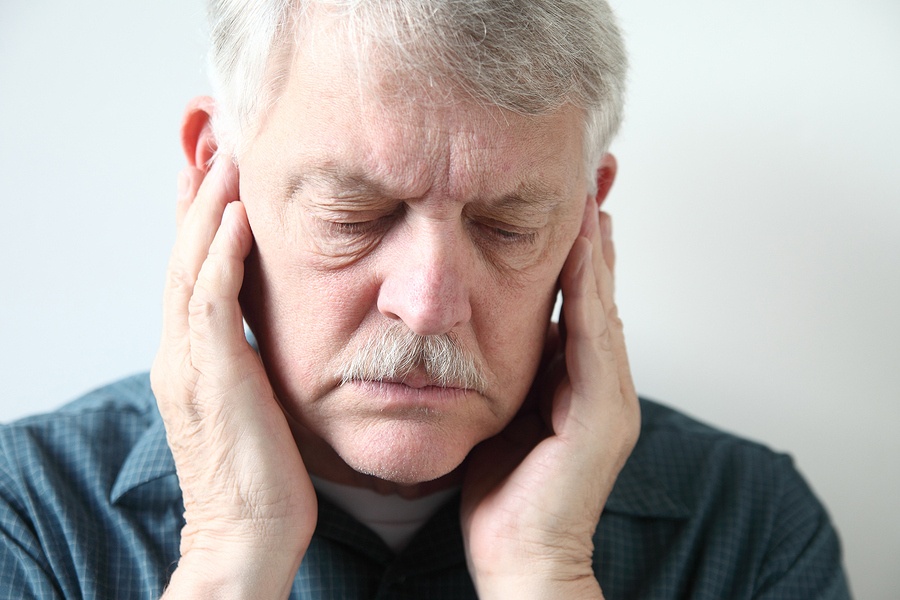 older man holds both hands to his upper jaw near the ears